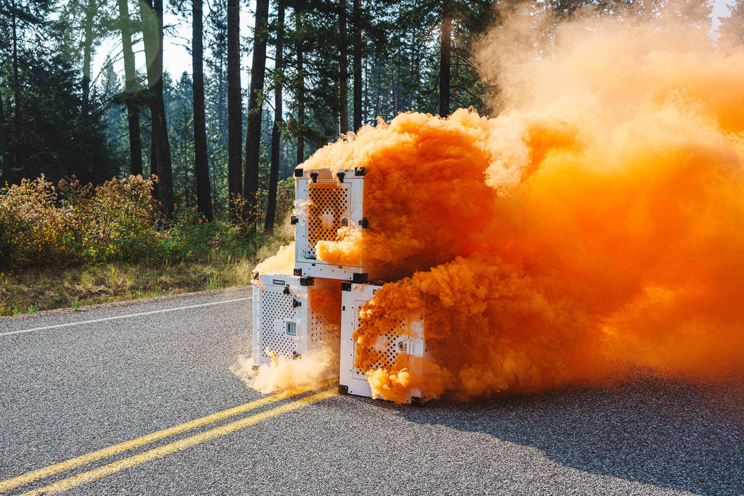 a photo of 3 dog crates stacked in a pyramid style with an orange smoke bomb inside of each one demonstrating the ventilation airflow