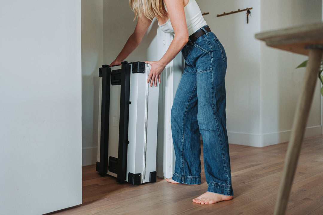 a woman placing a collapsed white collapsible dog crate in the closet demonstrating the space saving magic