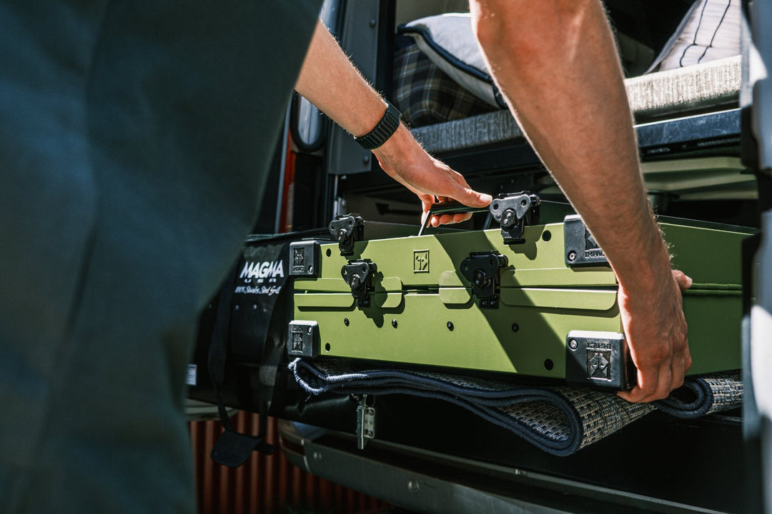 a man placing a folded compact od green collapsible dog crate in the back of a sprinter van demonstrating how its built for adventure and the ultimate travel crate